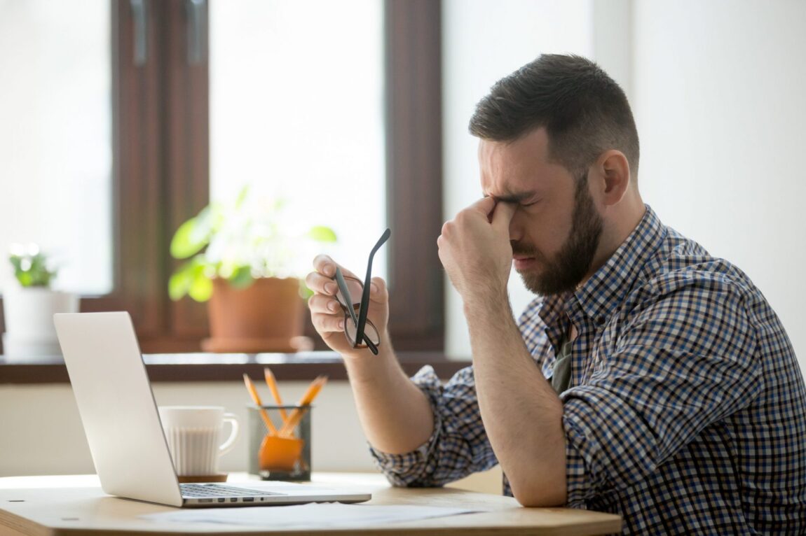 Photot of stressed man pinching the bridge of his nose illustrates blog: "Bouncing Back From Burnout"