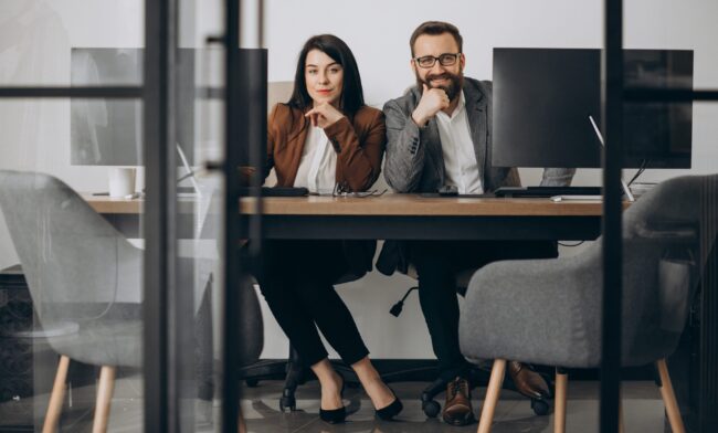 Two business partners working together in office Woman and man in business attire sitting side by side in office illustrate blog "Business Owner vs CEO: What Is the Difference?"