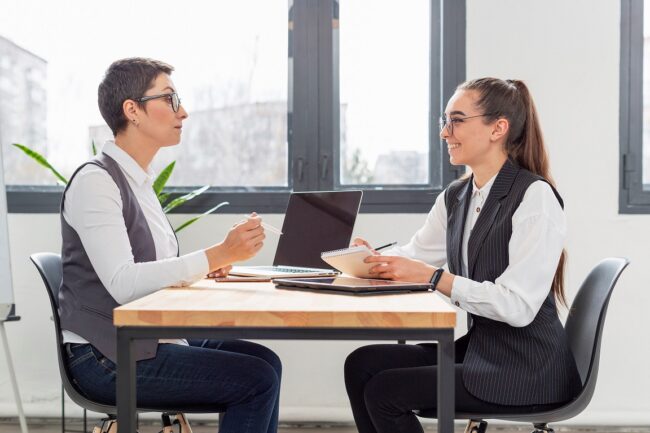 job-interview2-FP Two women in business attired sitting at a desk illustrate blog "Recruiting Tips for Small Businesses: How To Find the Right Candidates"