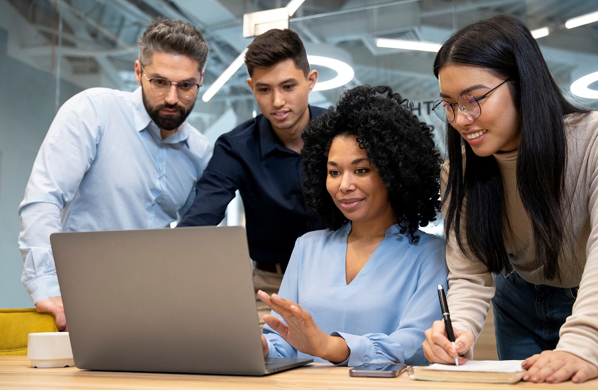 manager-FP Woman sitting in front of laptop with people around her illustrates blog "The 5 Most Common Management Pitfalls (and How To Avoid Them)"